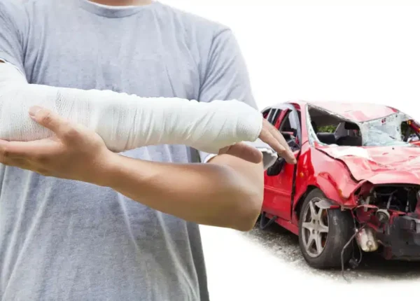 man with his arm in a cast standing in front of a wrecked car
