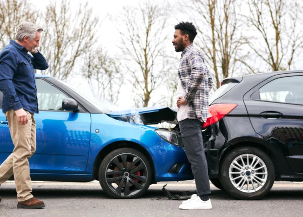 Two drivers look at their cars after a rear-end accident.