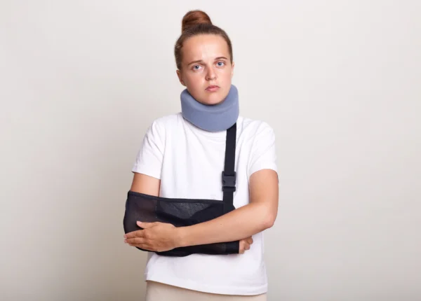 Injured woman wearing a sling and a neck brace looking hopelessly into the camera.