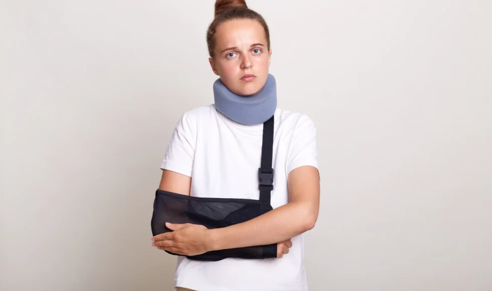 Injured woman wearing a sling and a neck brace looking hopelessly into the camera.