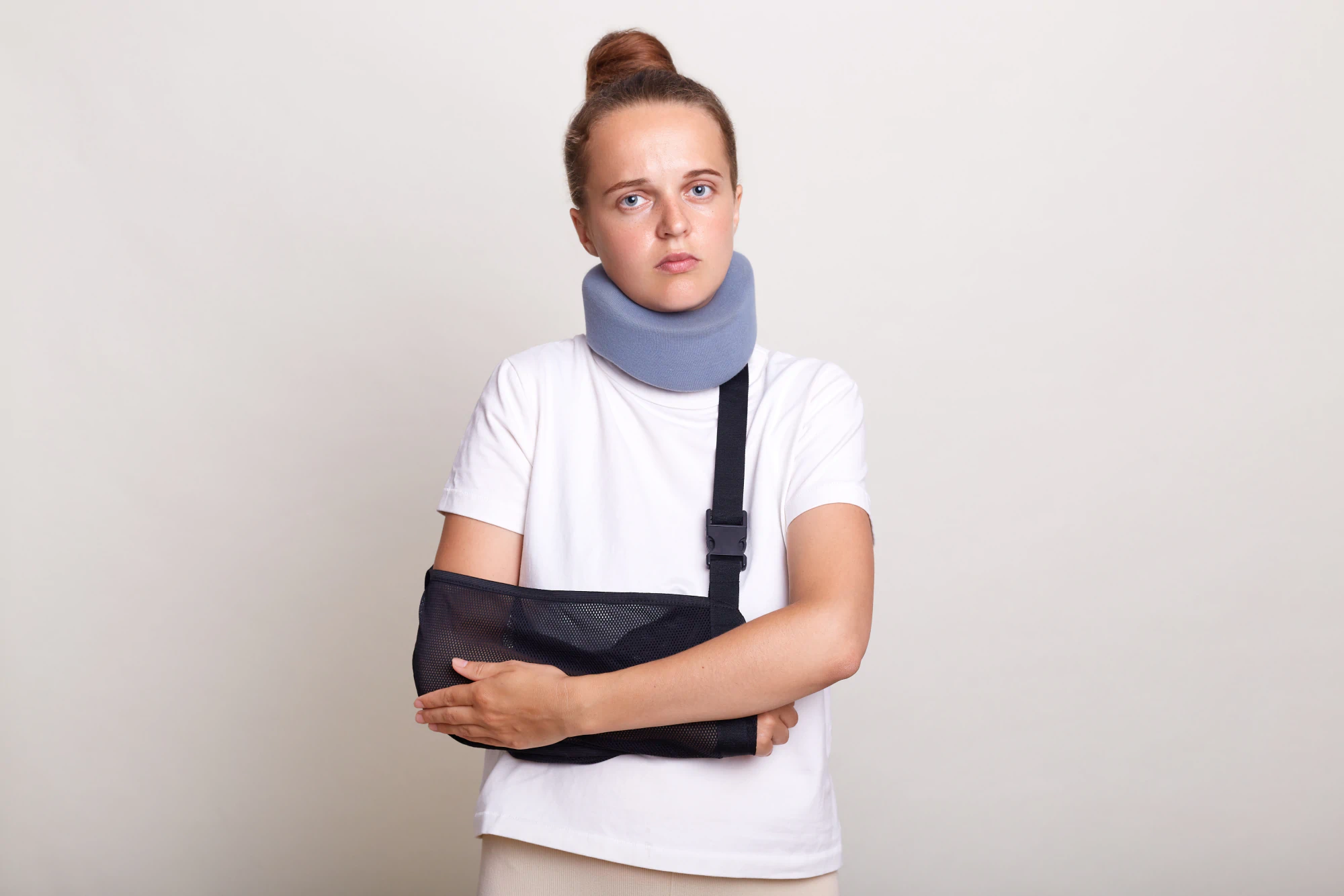 Injured woman wearing a sling and a neck brace looking hopelessly into the camera.