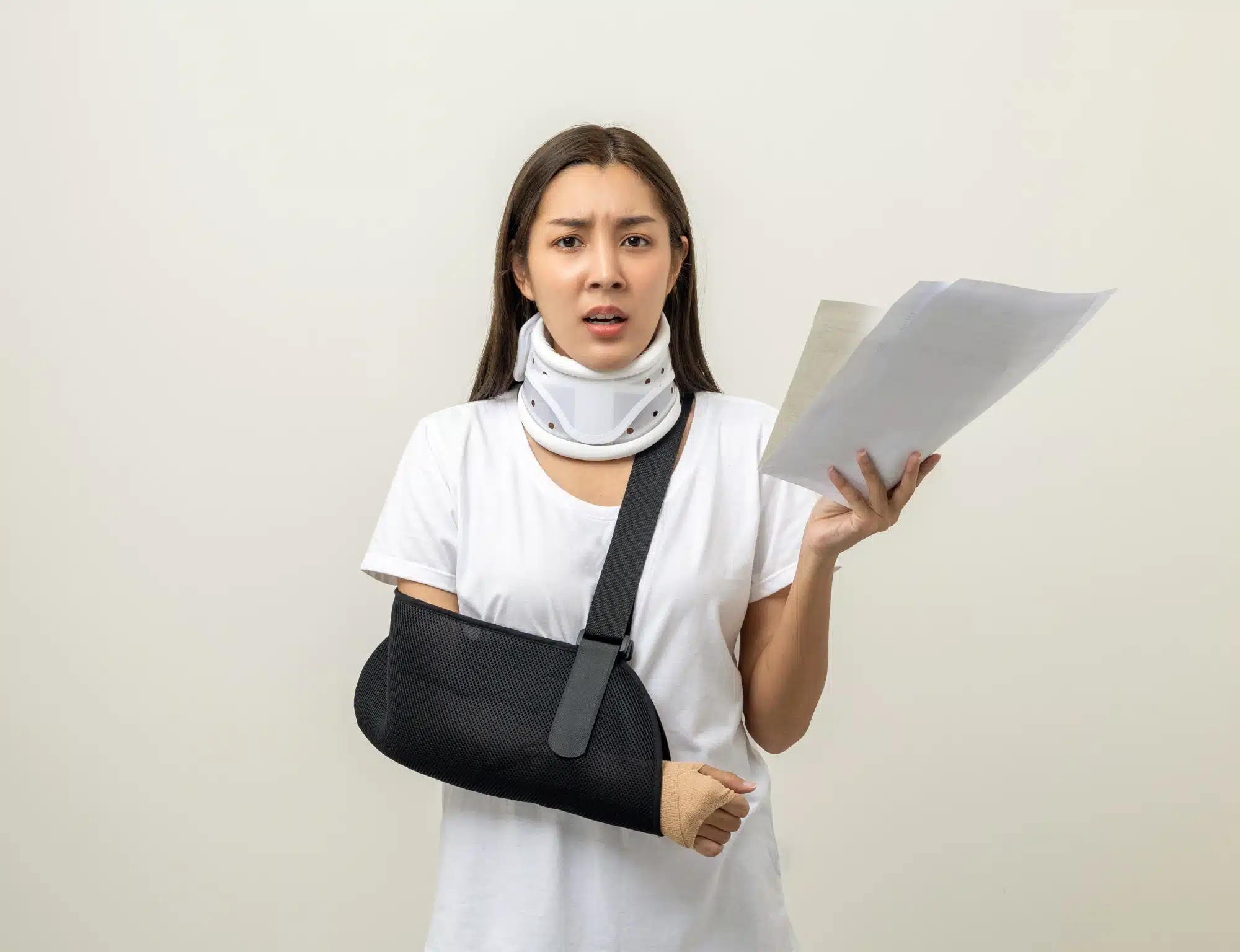 Woman in a neck brace and arm sling holding paperwork wearing a frustrated expression.