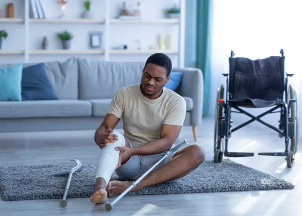 Young man sitting beside a wheelchair in his living room, leg in a cast.