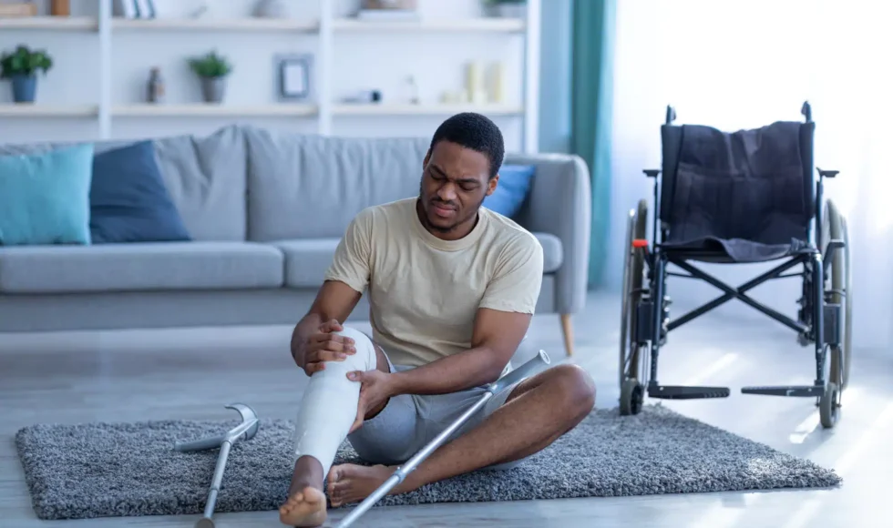 Young man sitting beside a wheelchair in his living room, leg in a cast.