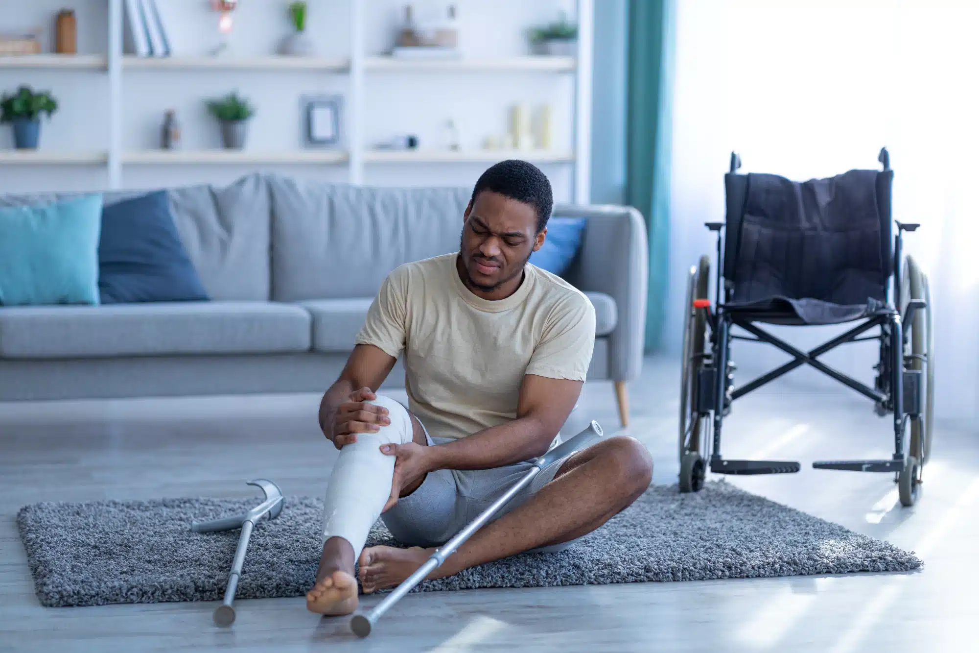 Young man sitting beside a wheelchair in his living room, leg in a cast.